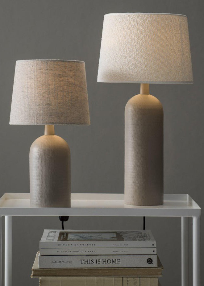 Två beige bordslampor med strukturerad keramisk fot och tygskärmar i en minimalistisk miljö.