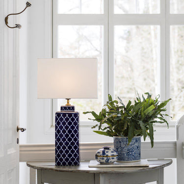 Elegant bordslampa med mönstrad blå fot och vit skärm, perfekt för fönsterbänk eller sidobord i vardagsrum.
