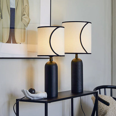 Två svarta bordslampor med vita skärmar på mörkt sidobord