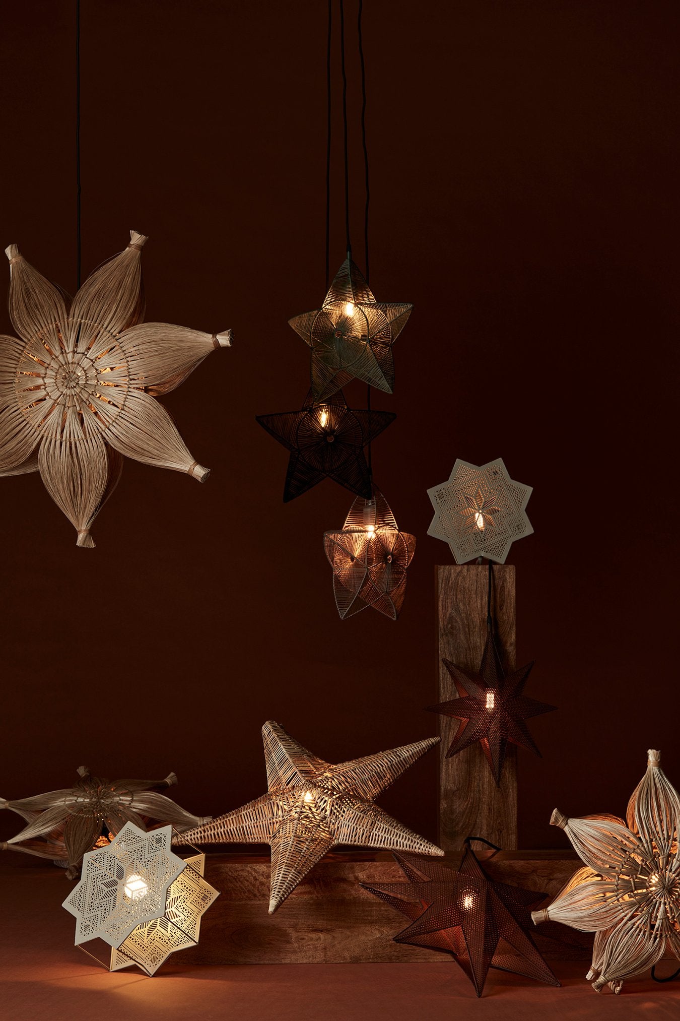 Julstjärnor i olika former och material lyser stämningsfullt mot en varm brun bakgrund.