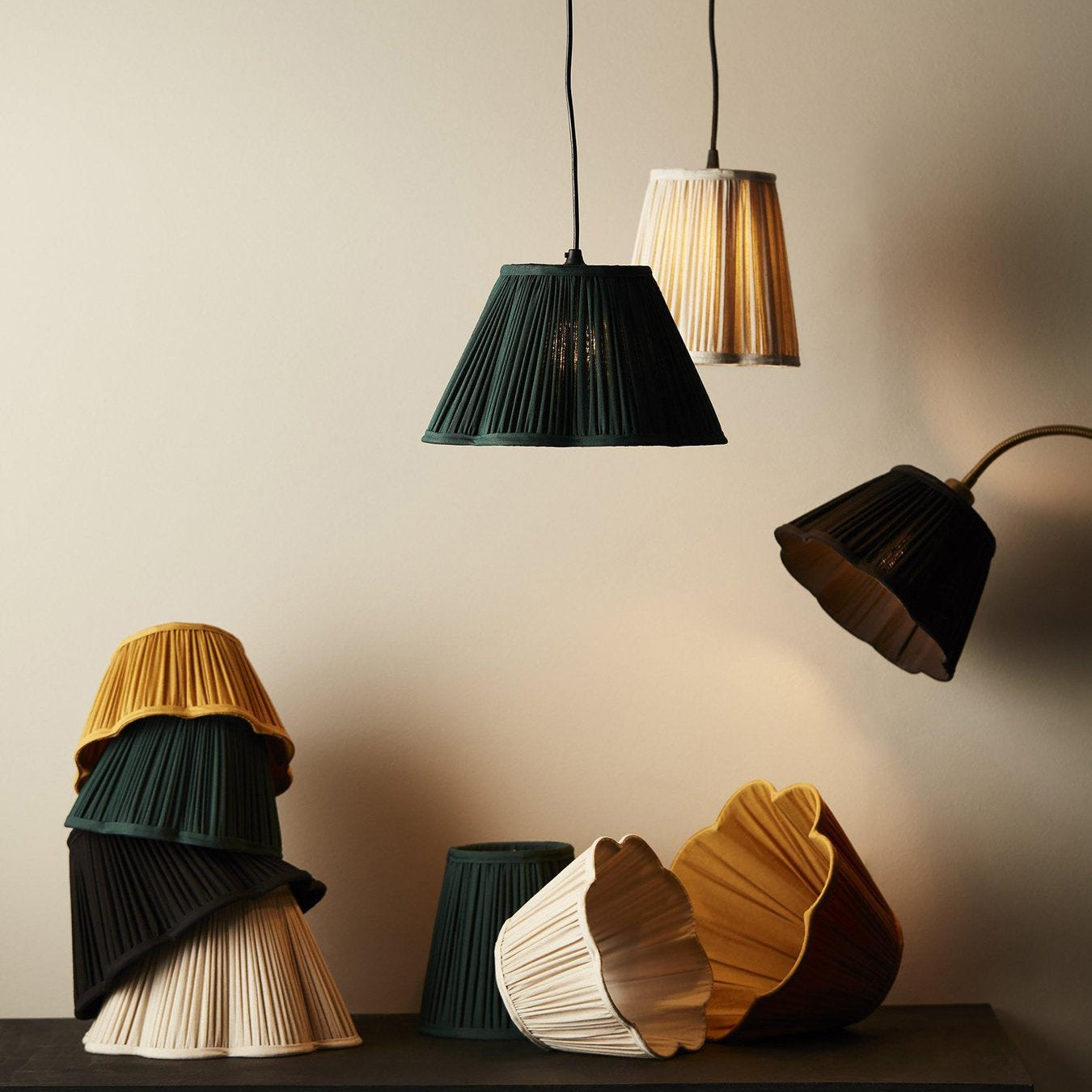 Veckade lampskärmar i tyg i färgerna grön, gul och vit, både hängande och stående på bord.
