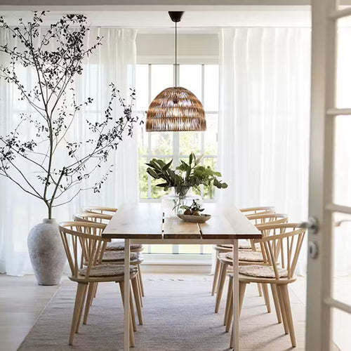 Flätad taklampa ovanför matbord i ljust matsalsrum med stora fönster
