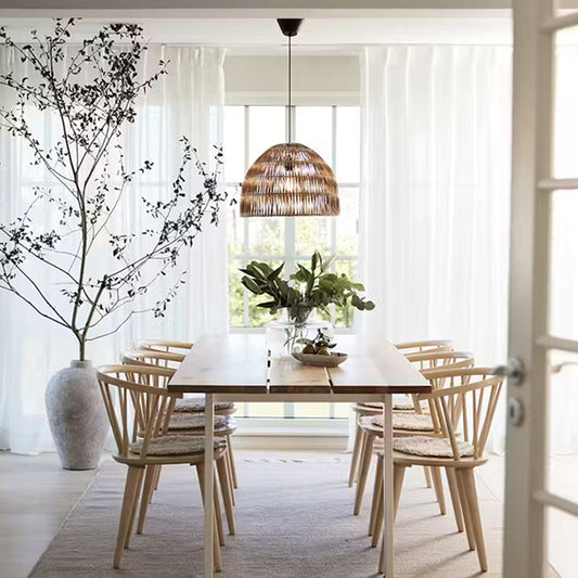 Flätad taklampa ovanför matbord i ljust matsalsrum med stora fönster