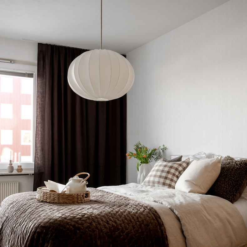 Sovrum med vit rund taklampa och mörka gardiner i bakgrunden
