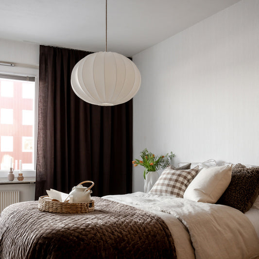 Sovrum med vit rund taklampa och mörka gardiner i bakgrunden