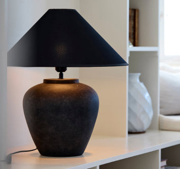 Svart bordslampa med klassisk design på vit hylla i ljus inomhusmiljö