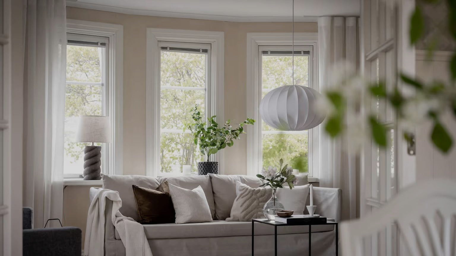 Ljust och luftigt vardagsrum med taklampa i skandinavisk design, soffgrupp i neutrala toner och gröna växter i fönstret.